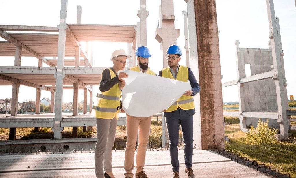 Three architects examine plans on construction site